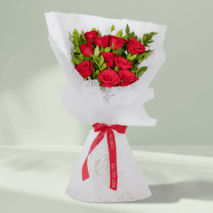Vibrant red roses with fresh green leaves, elegantly wrapped in white non-woven paper and tied with a bright red satin ribbon.