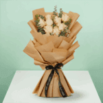 Peach roses artfully arranged with eucalyptus, wrapped in brown non-woven paper, and tied with a black satin ribbon.