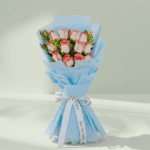 A bouquet of 12 white roses with green leaves, wrapped in bright fuchsia pink non-woven paper and tied with a white and black ribbon.